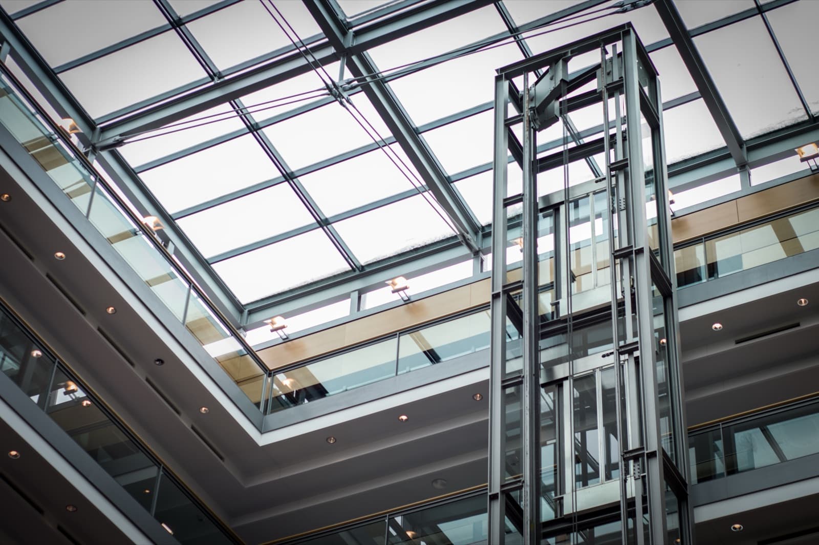 Glass lift shaft rising through a skylit office atrium