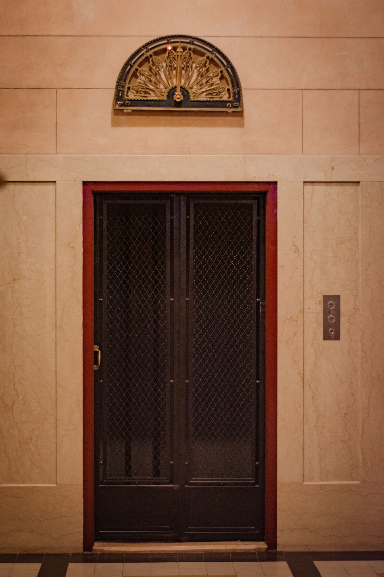 Latticed lift doors beneath a brass floor indicator